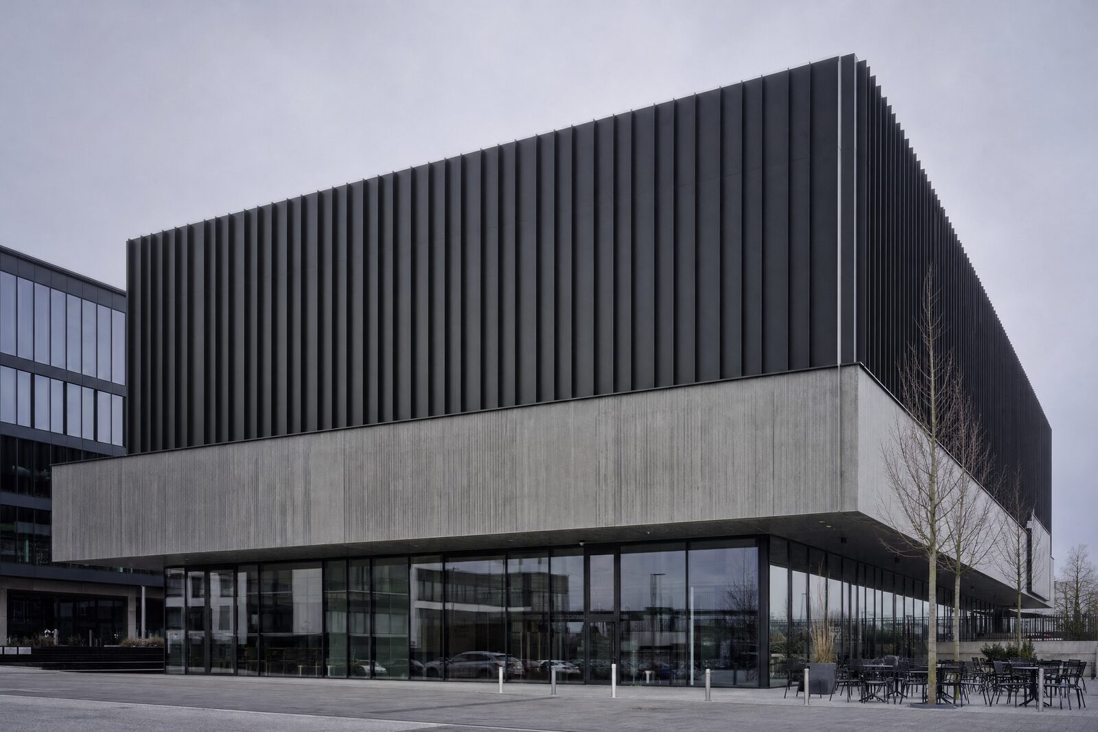 Gebouw met een gesloten zaalvolume boven een transparante plint met bedrijfsruimtes en een horecazaak
