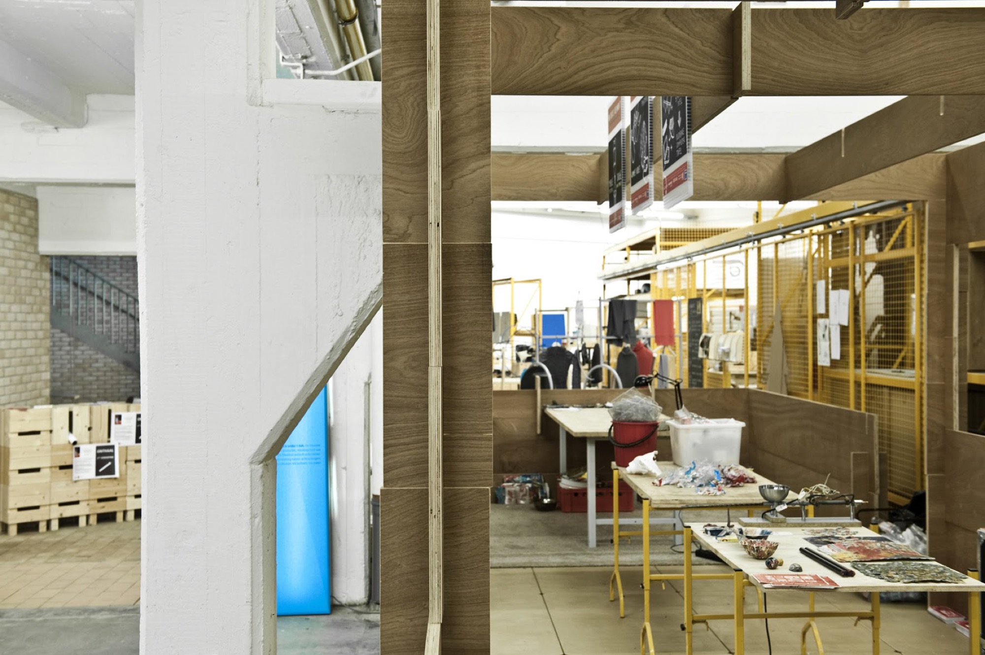 Doorkijk tussen de houten modules van BUDA.lab naar de open werkplaats met werktafels en gele rekken