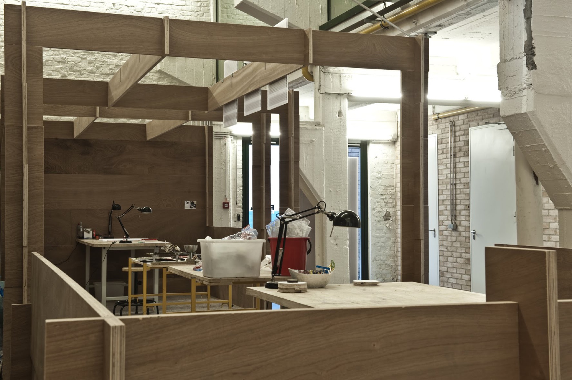 Houten moduleframe van BUDA.lab opgebouwd in de fabriekshal, met werktafels erachter en de bestaande witgeschilderde structuur