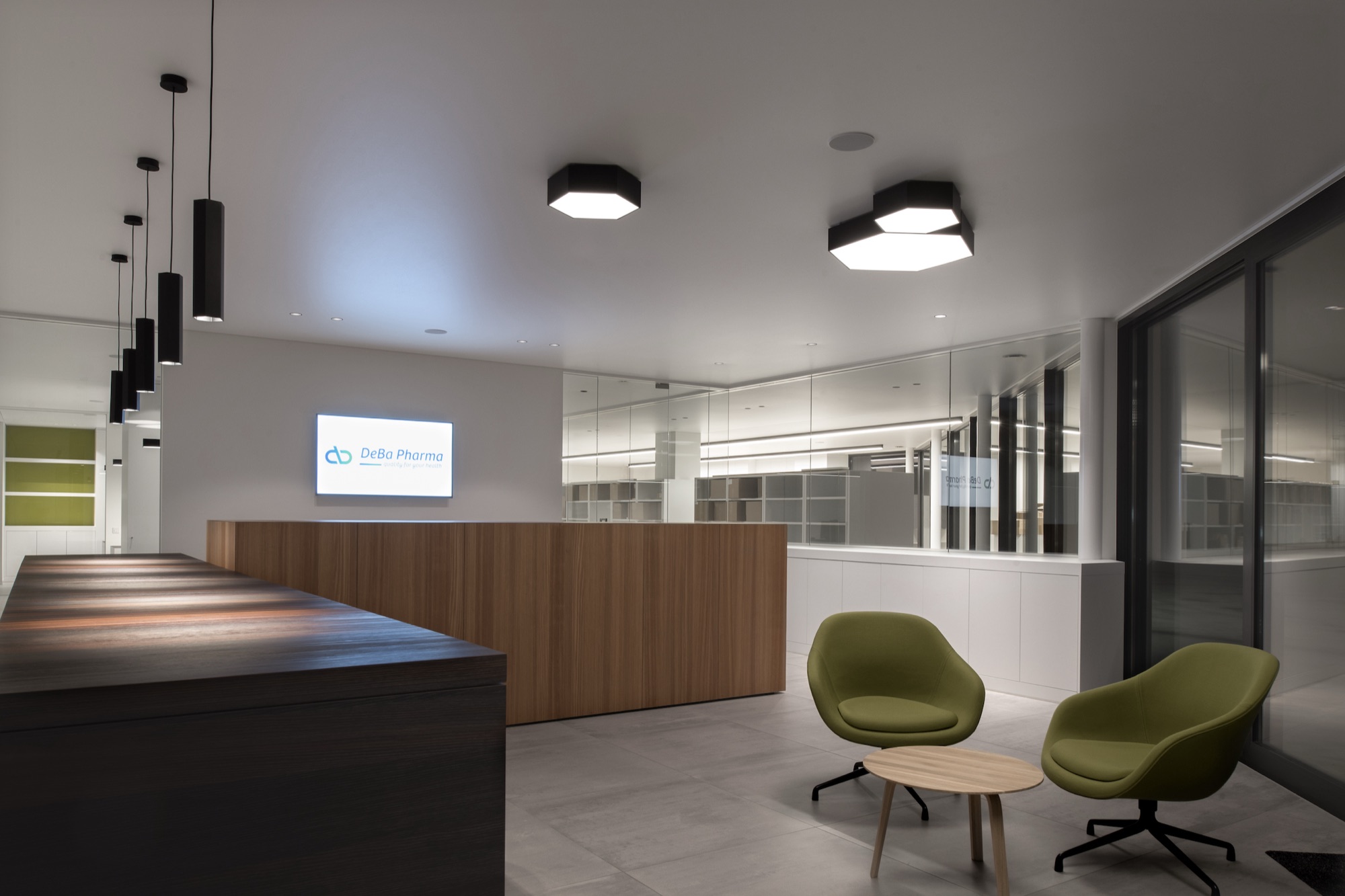 Onthaal van DeBa Pharma met een houten balie, een verlicht logopaneel, groene fauteuils en een glazen scheidingswand naar de kantoren