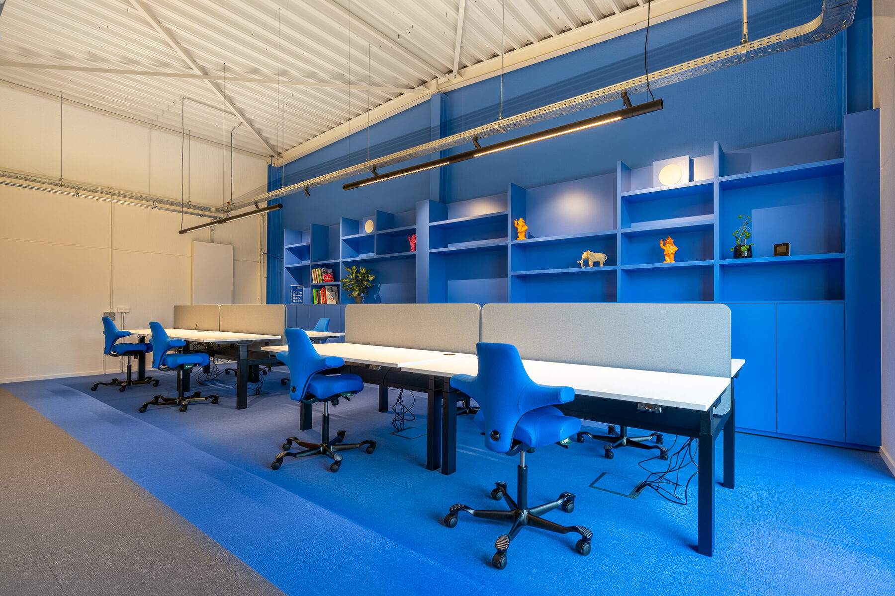 Blauwe werkzone bij GBL Agency met blauw tapijt, een blauwe maatkast met open vakken en een rij bureaus met blauwe stoelen
