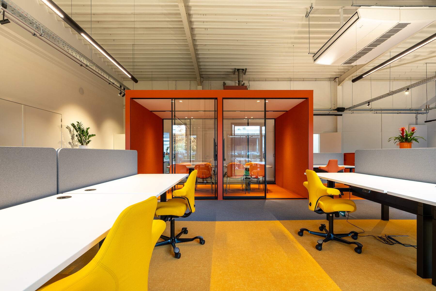 Vrijstaand oranje overlegvolume midden op de werkvloer van GBL Agency, met gele bureaustoelen links en rechts