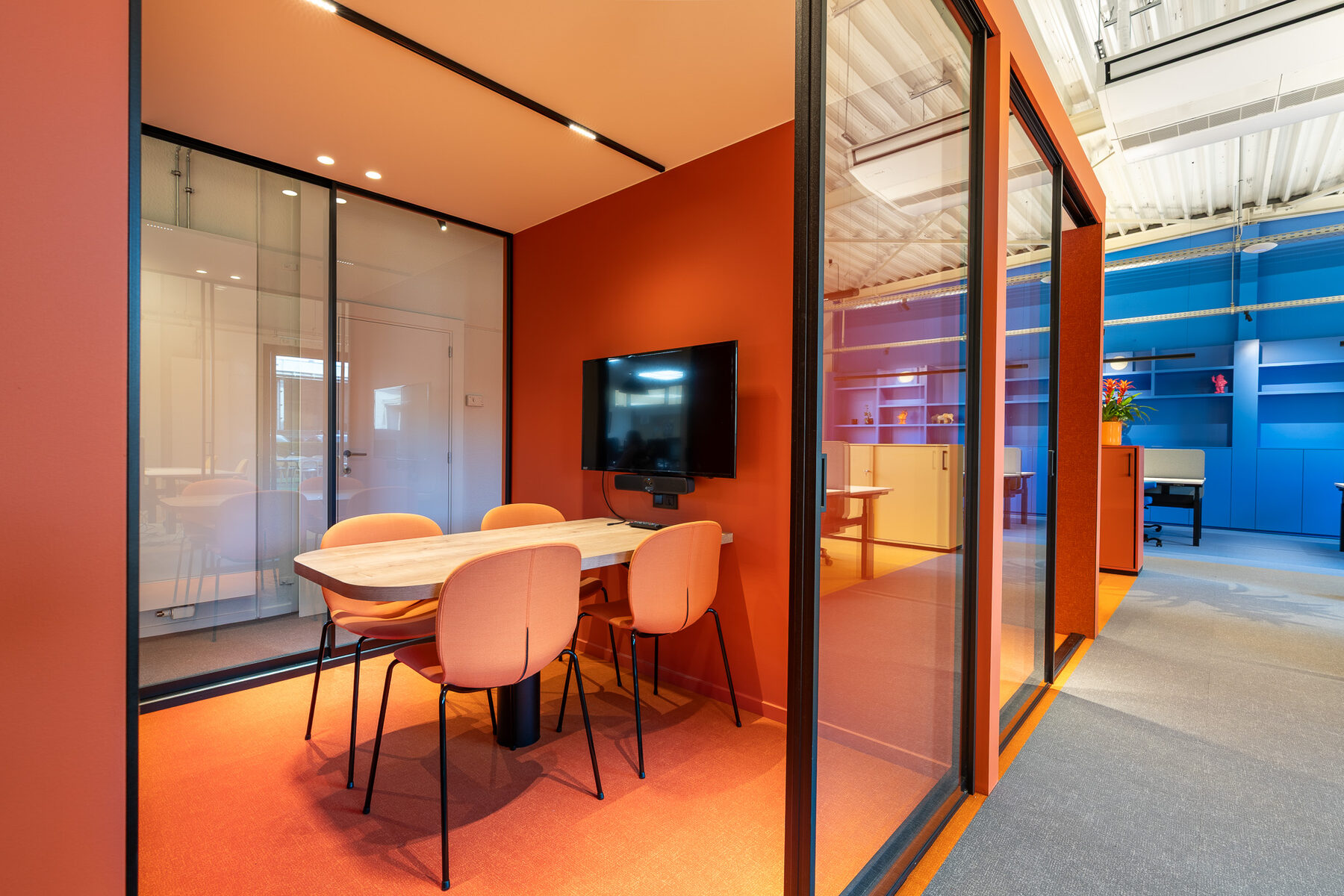 Afsluitbare overlegruimte bij GBL Agency achter glas in zwart profiel, met oranje wanden, een scherm en oranje stoelen