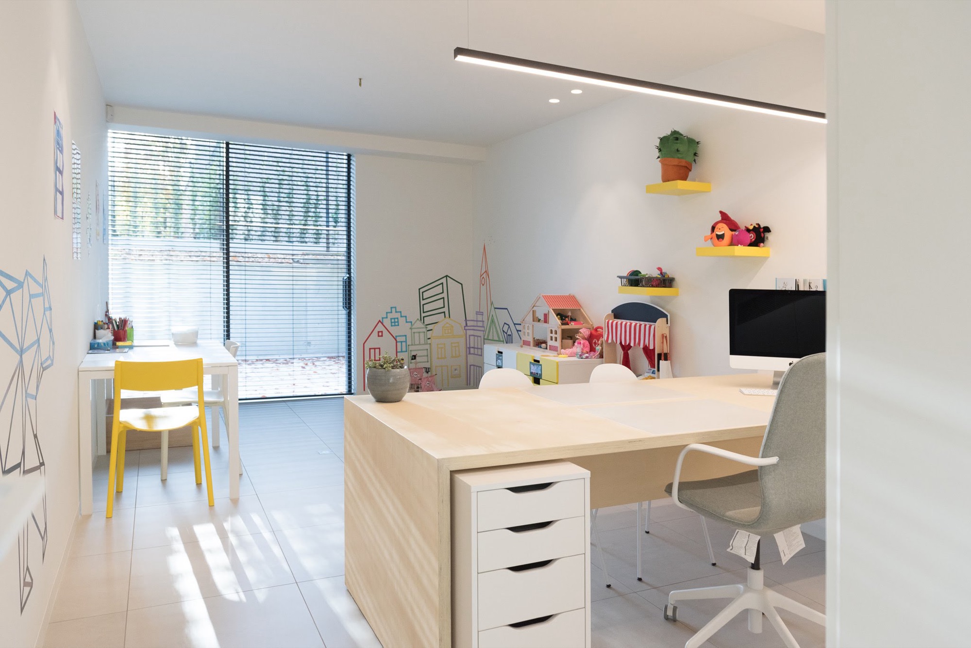 Kabinet in Groepspraktijk Tille met een houten bureaublok, een aparte kindertafel met gele stoeltjes en speelgoed op wandplanken