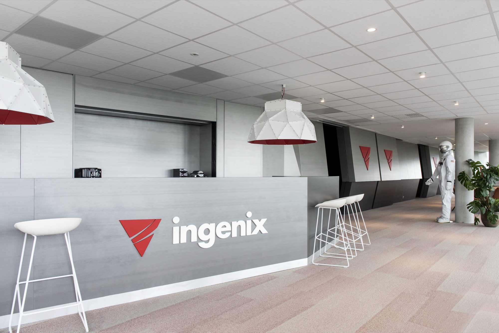 Onthaalzone van Ingenix met balie, witte krukken, hanglampen en de gang met wandpanelen die naar achteren doorloopt