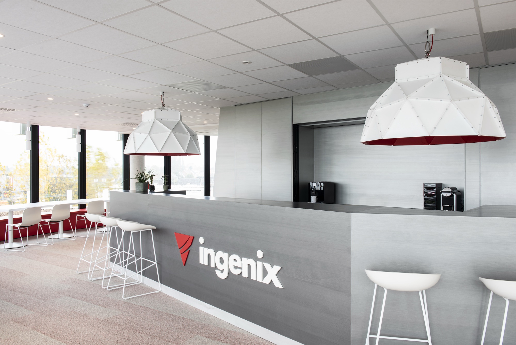 Onthaalbalie van Ingenix in grijs met rood logo, witte krukken ervoor en grote gefacetteerde hanglampen met rode binnenzijde erboven