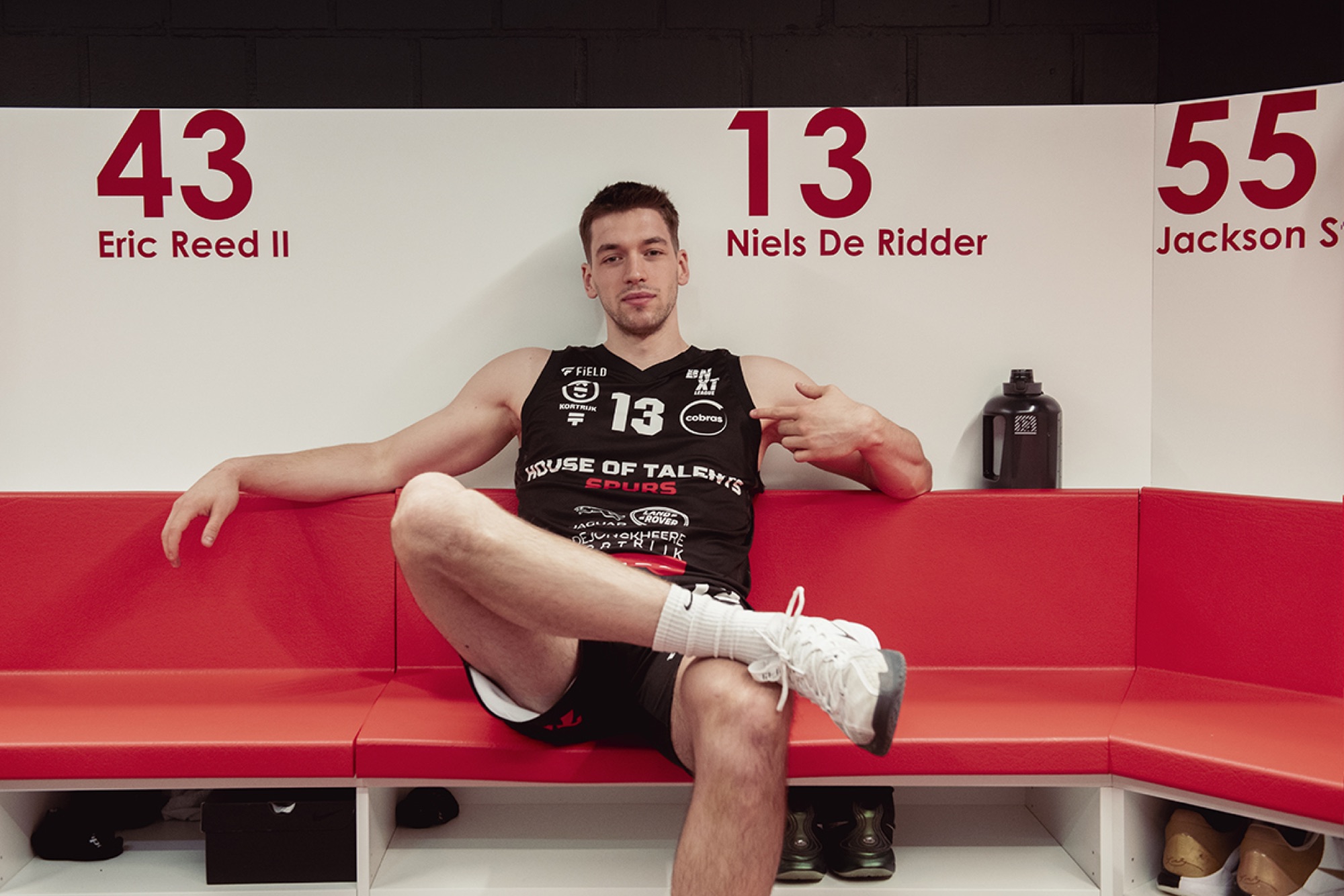 Speler van de Kortrijk Spurs op de rode zitbank onder de wand met rugnummers 43, 13 en 55