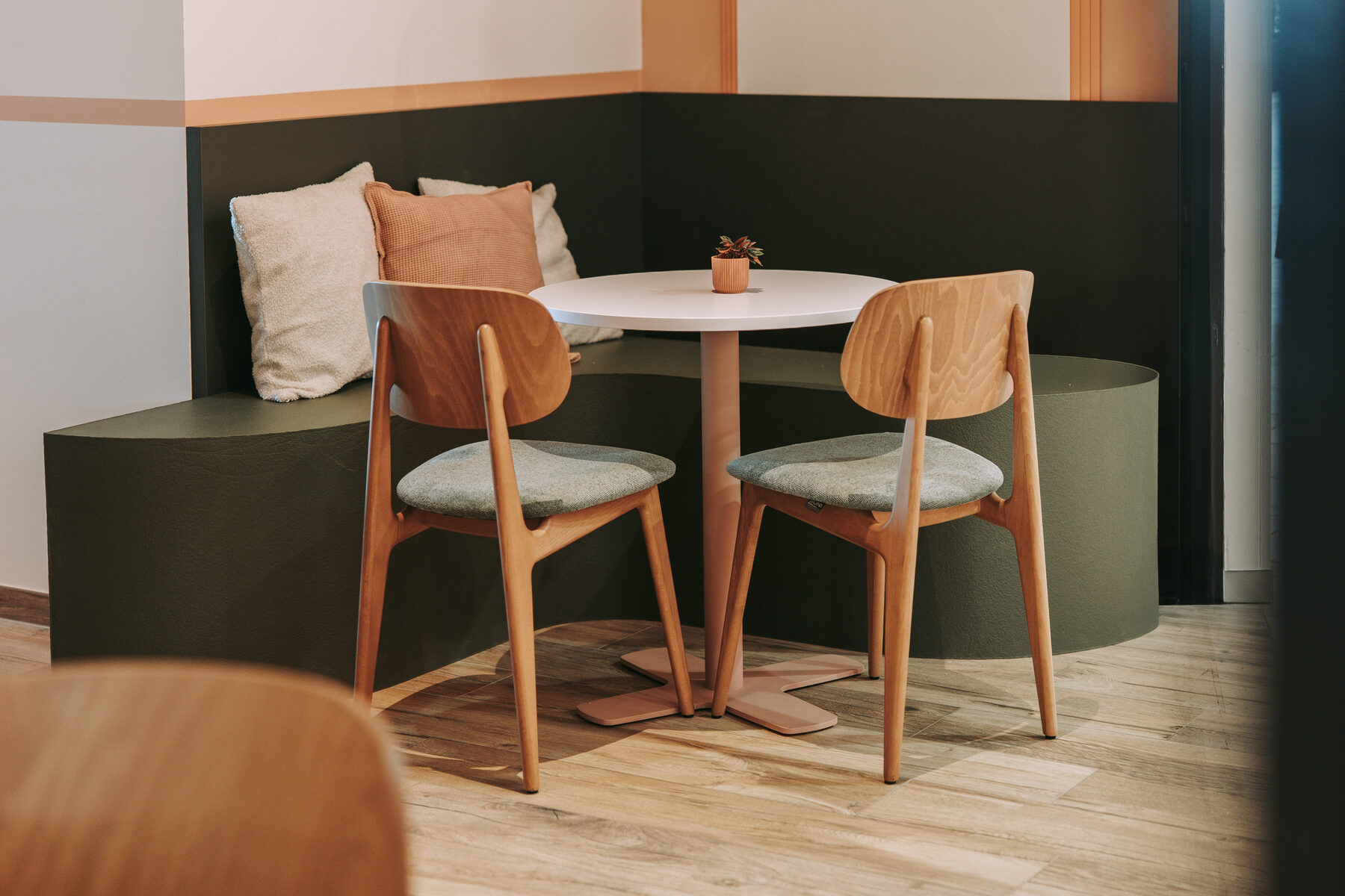 Zithoek bij Madame Croqu'o met een donkergroene gestoffeerde hoekbank met kussens, een ronde witte tafel en twee houten stoelen op een houten vloer