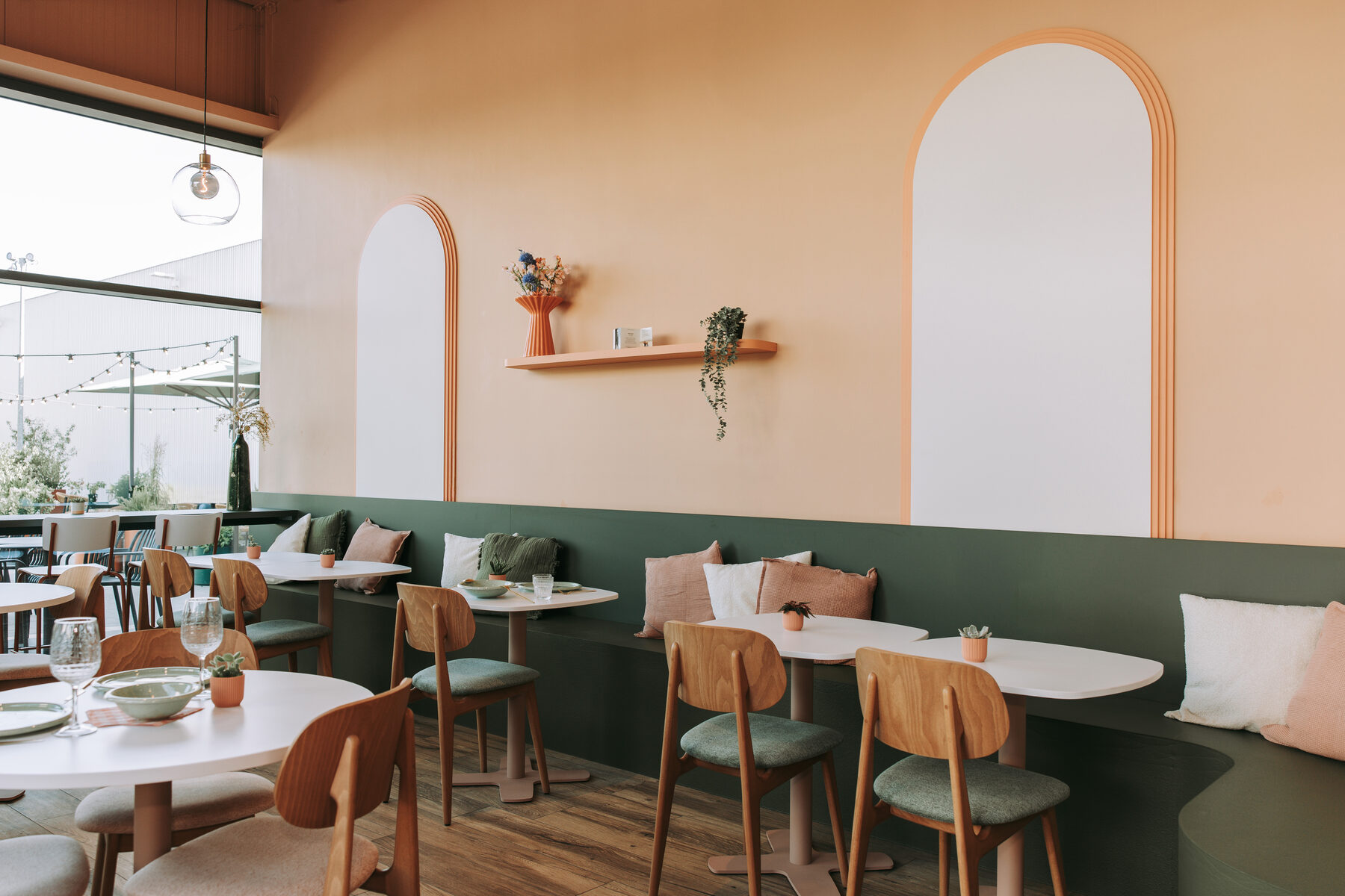 Zaal van Madame Croqu'o met een doorlopende groene wandbank, ronde witte tafels, houten stoelen en twee witte boognissen in de wand