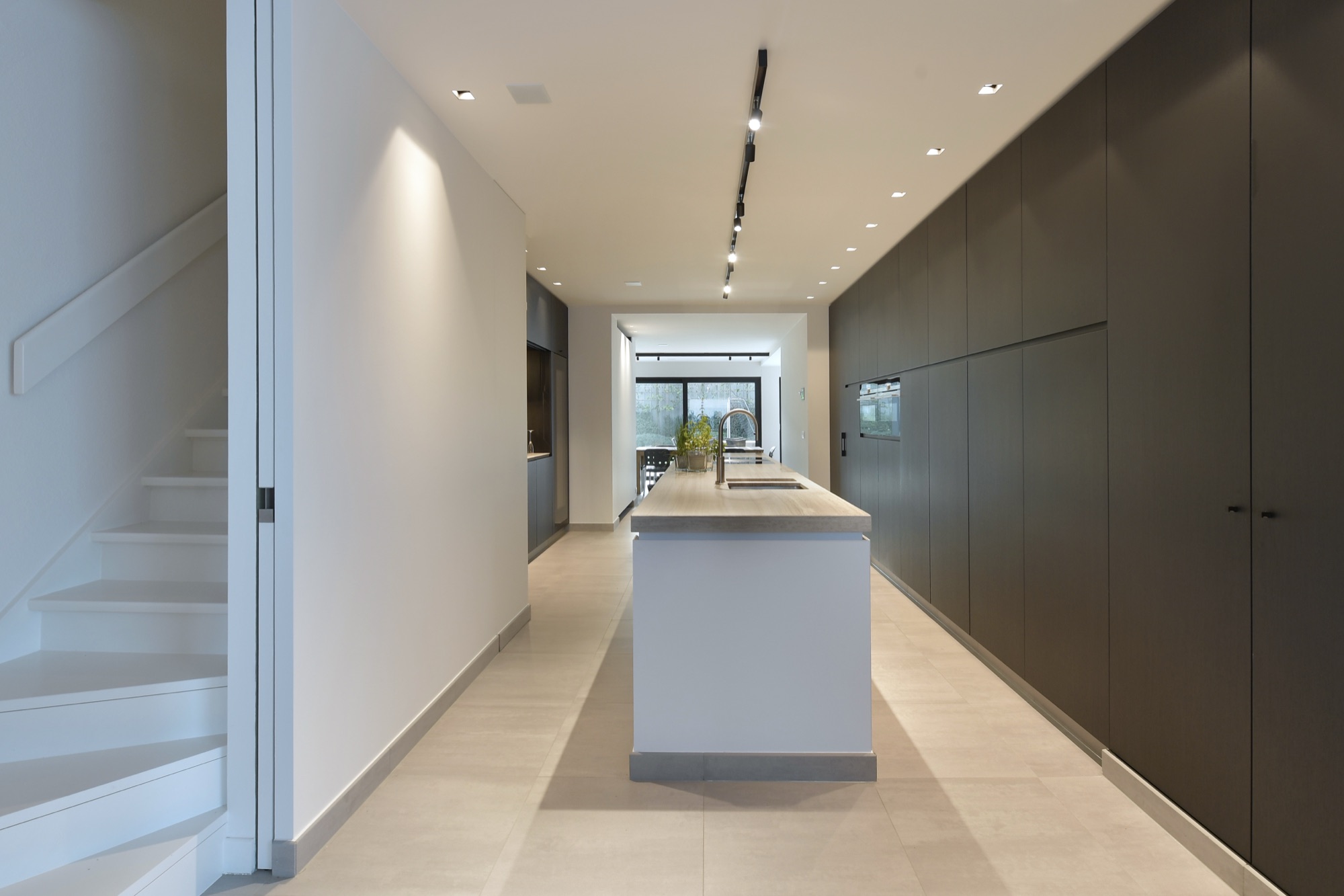 Doorlopende ruimte in Narrow House met een witte trap links, een donkere kastenwand rechts en het keukeneiland in het midden