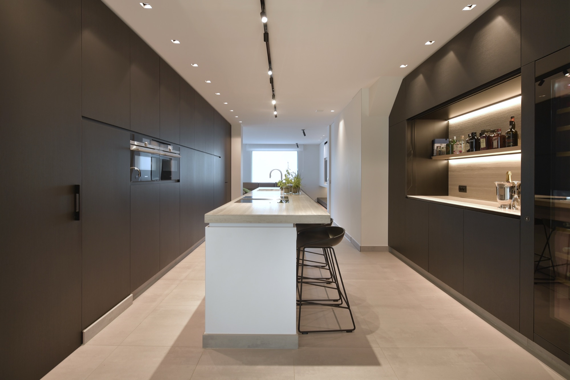 Keuken van Narrow House met een volledig donkere kastenwand met ingebouwde ovens en het lichte keukeneiland ervoor