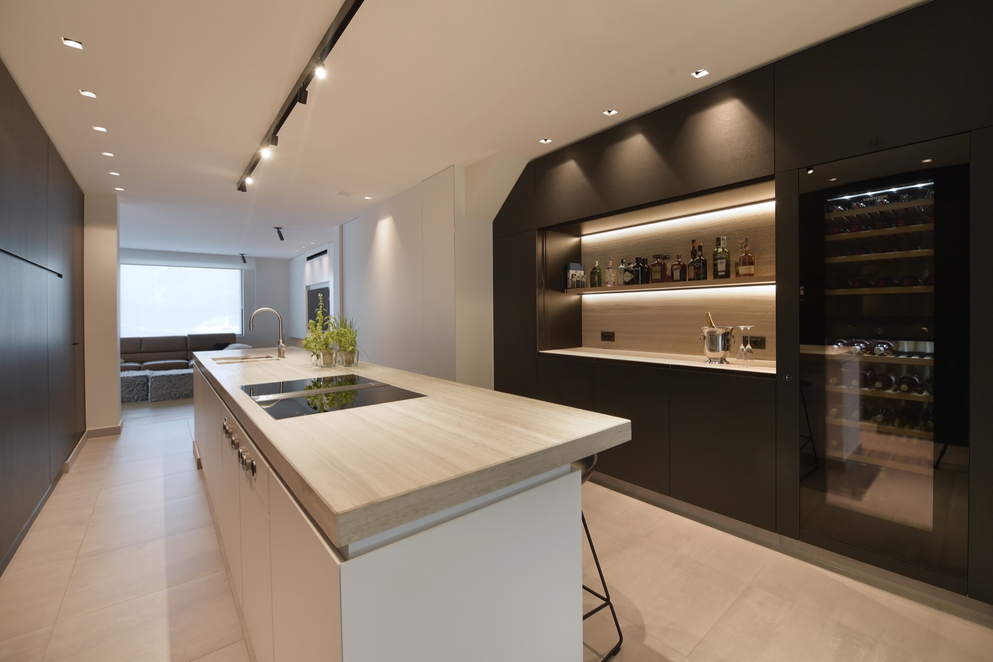 Keuken van Narrow House met een keukeneiland met licht blad, een donkere achterwand met verlichte nis en een ingebouwde wijnkast