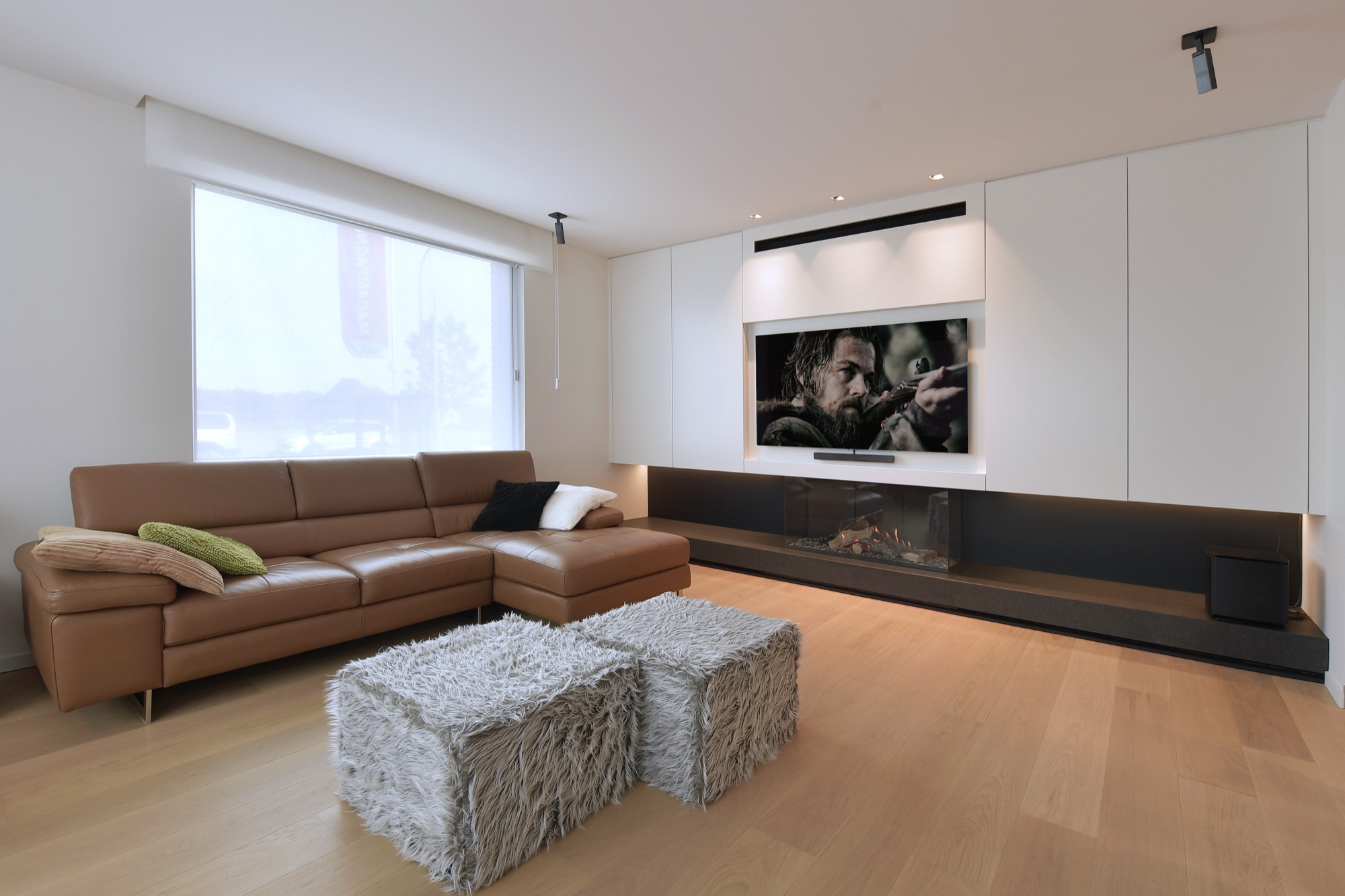 Leefruimte van Narrow House met een leren hoeksalon, een ingewerkte haard onder een tv in een witte kastenwand en een eiken vloer