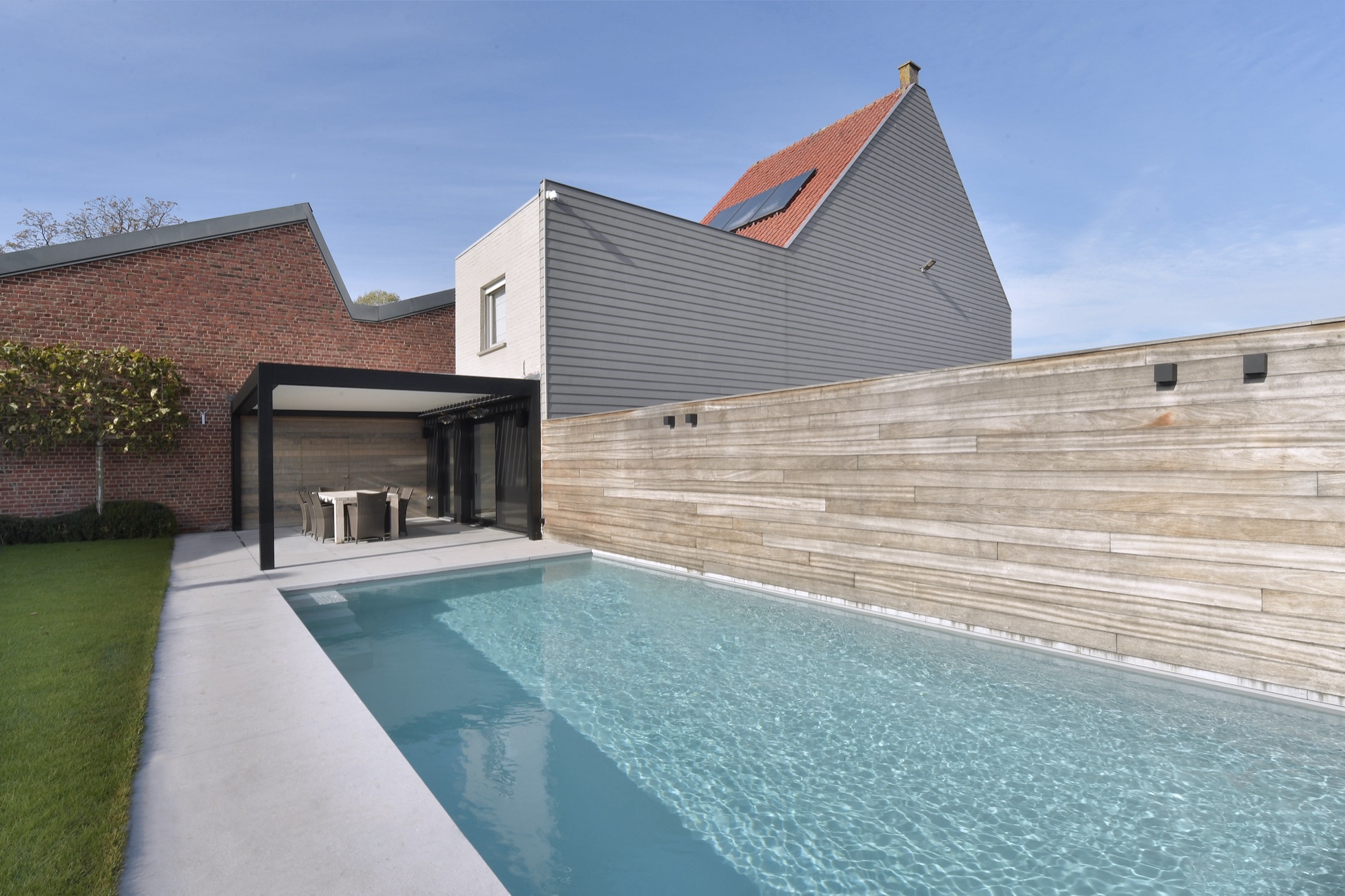 Tuin van Narrow House met een langwerpig zwembad, een overdekt terras tegen de achterbouw en een tuinmuur in lichte steenstrips