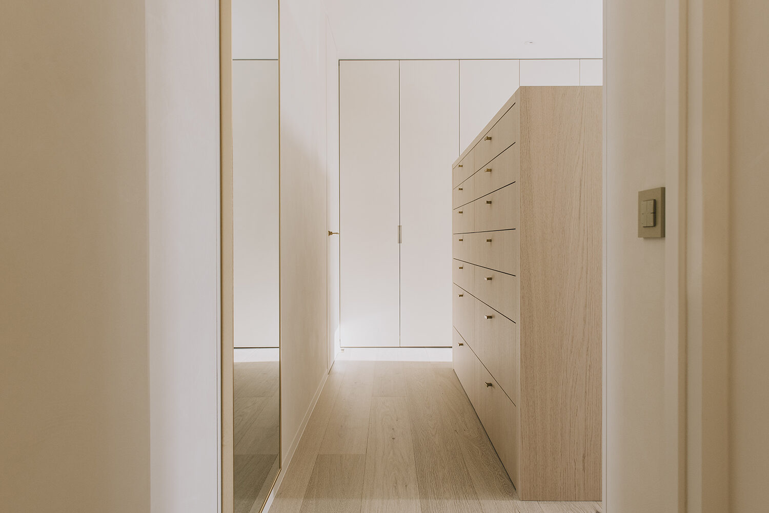 Dressing in het appartement in Nieuwpoort met een hoge spiegel links, een ladenkast in licht eik en een gesloten kastenwand in het verlengde, op een lichte houten vloer