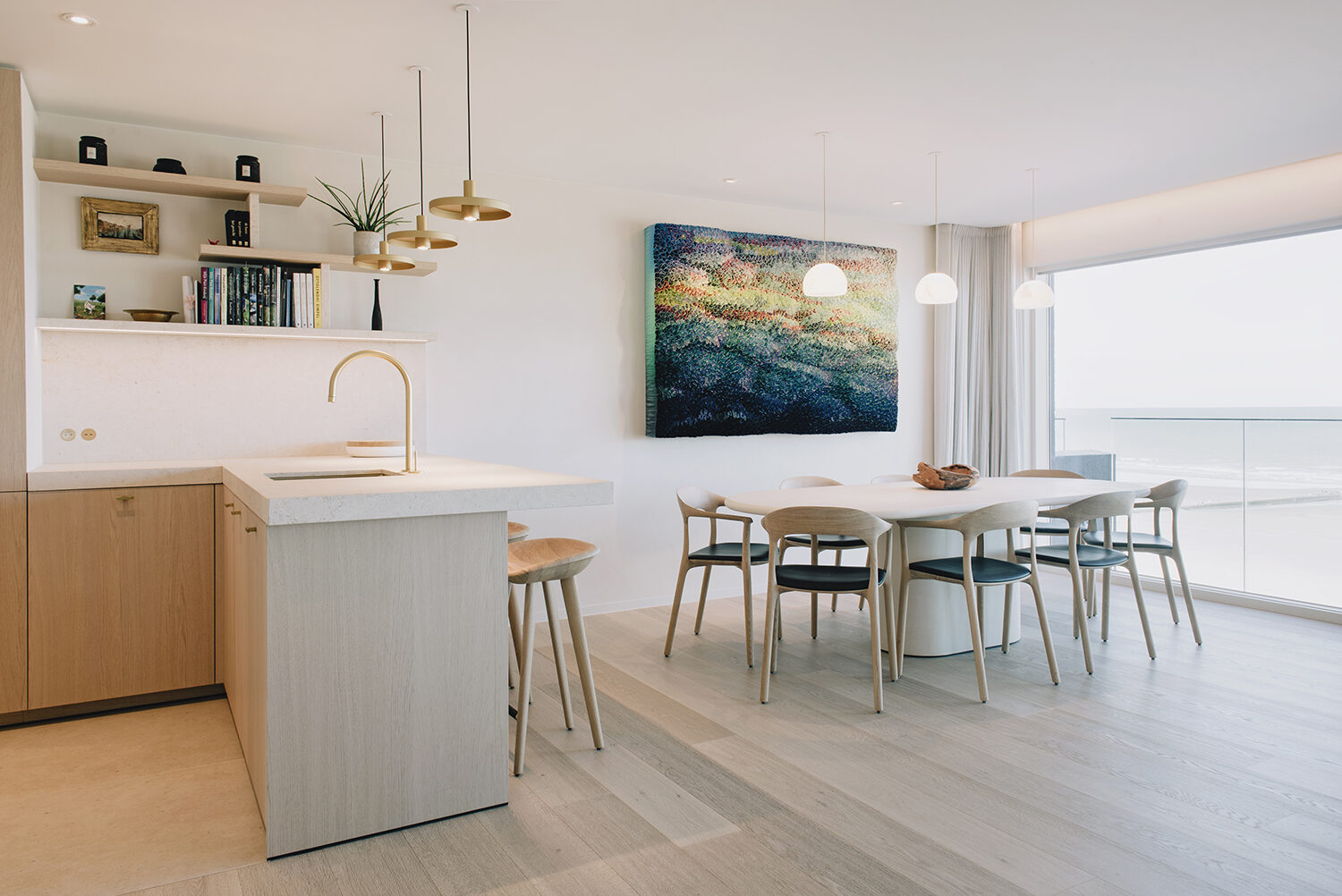 Eetruimte van het penthouse in Nieuwpoort met ovale eettafel en stoelen, een keukeneiland in licht eik en zeezicht door de raampartij rechts