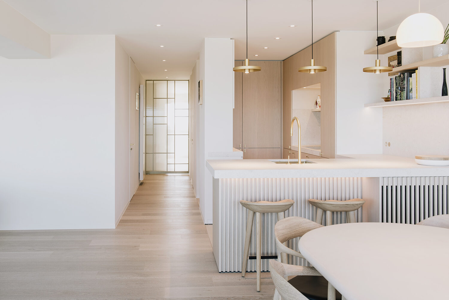 Keukeneiland met geribde voorzijde en twee krukken in het appartement in Nieuwpoort, met een lange gang met kastenwand ernaast